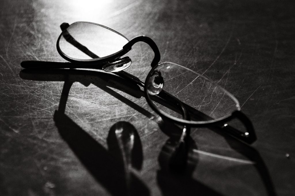 Black and white photo of eyeglasses with shadow on a reflective surface.