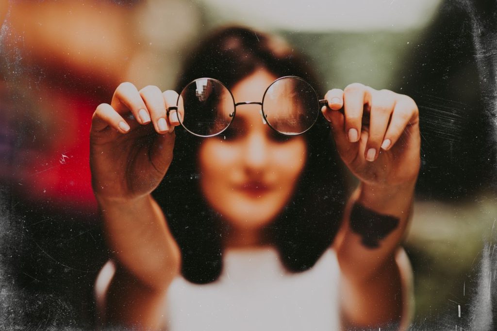 Blurred artistic photo of a woman holding eyeglasses in focus.