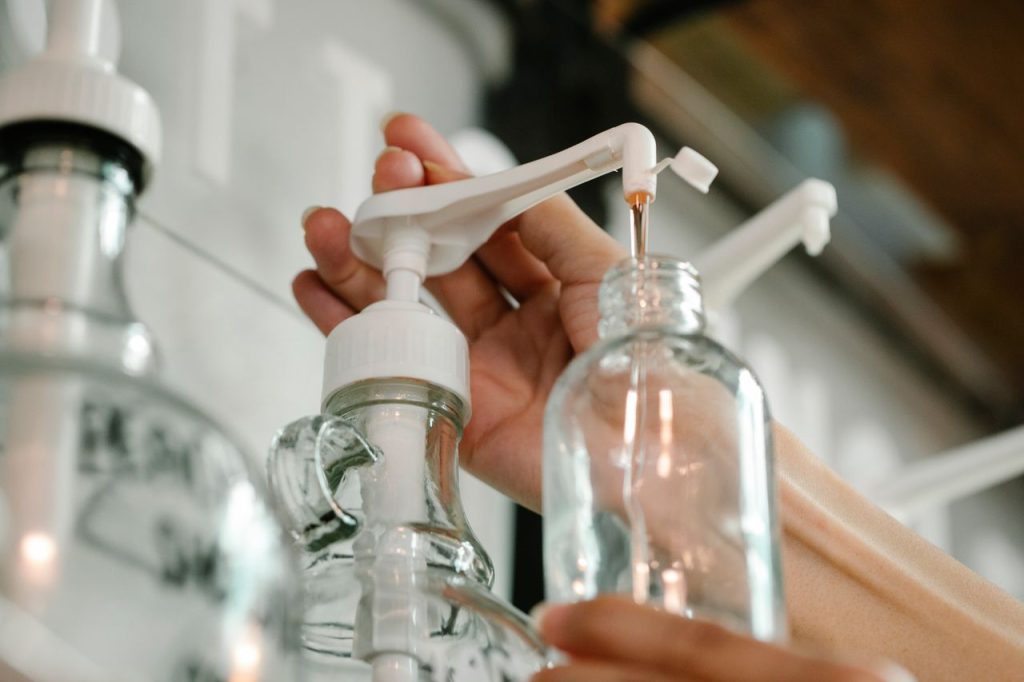 Crop unrecognizable person pushing and pouring soap from dispenser to plastic bottle